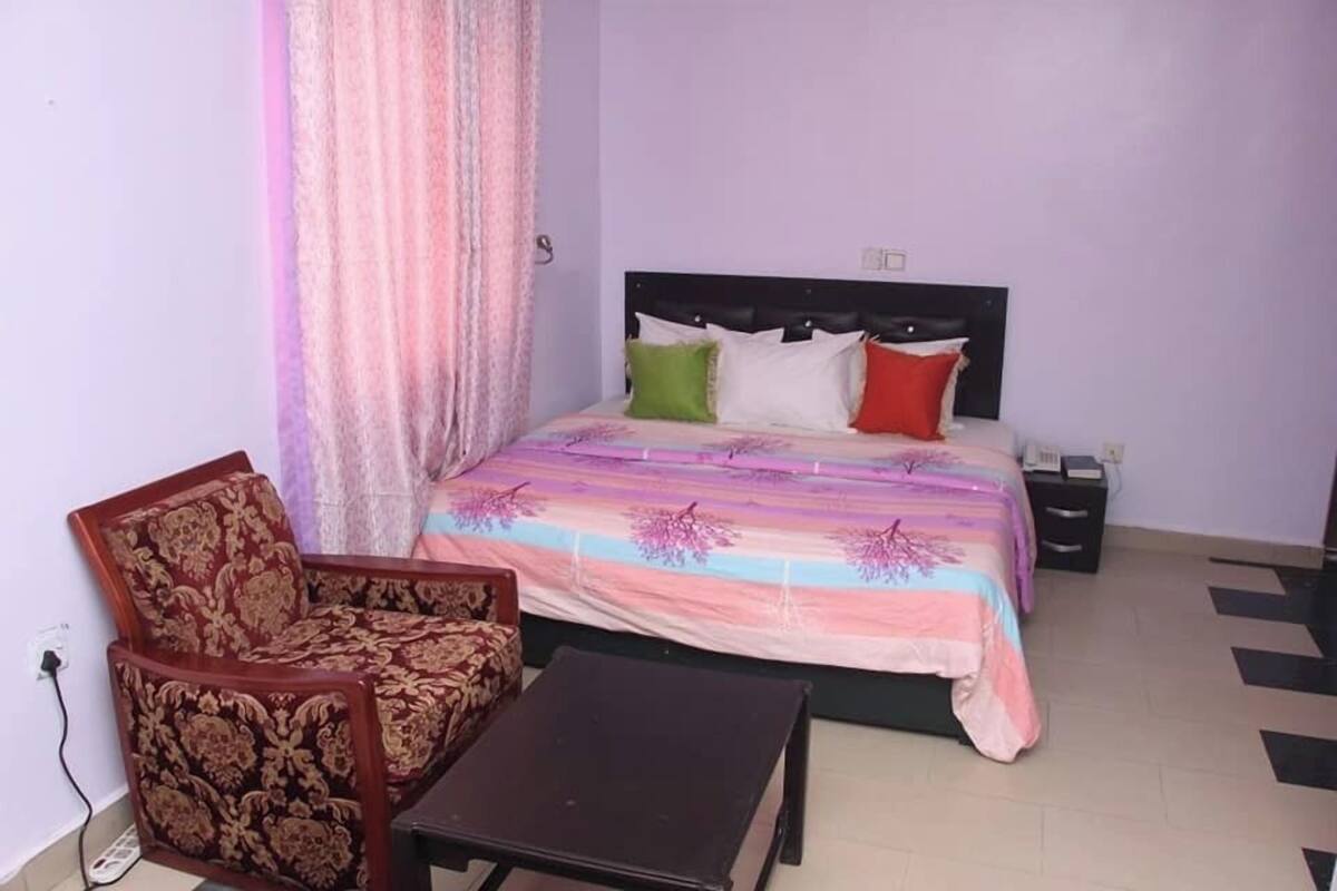 A bedroom with a bed, a chair, a nightstand, and a small table.