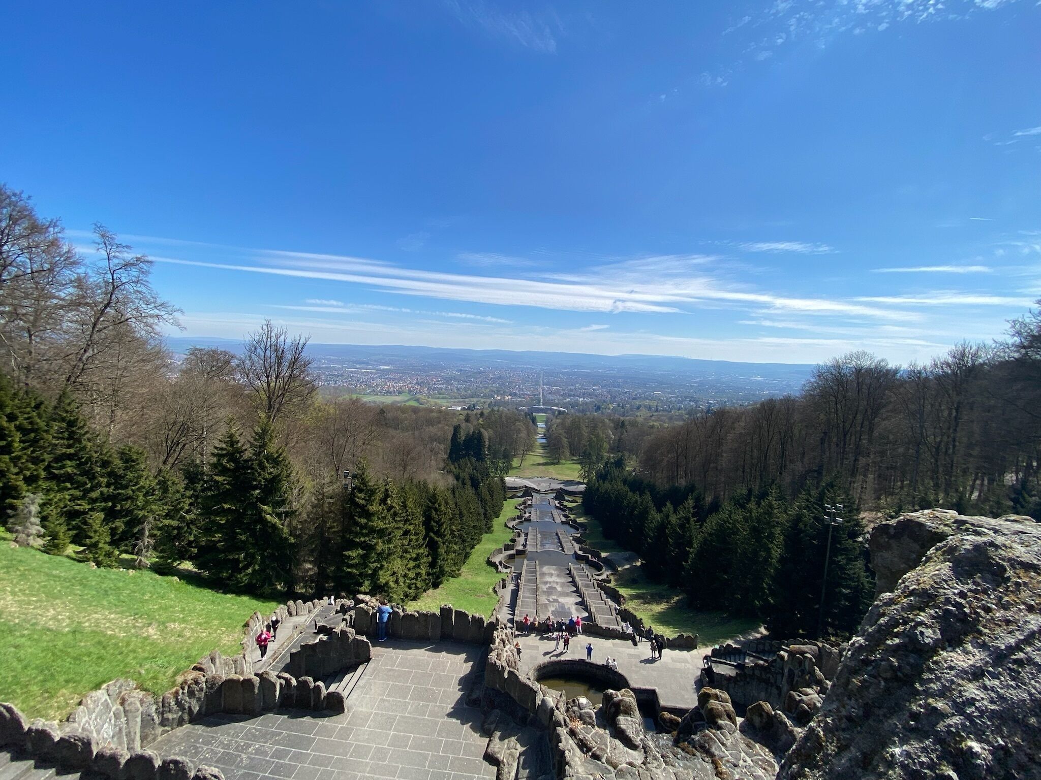 Eine historische Stätte mit einem zentralen Weg, Steinbauten und Blick auf eine ferne Stadt.