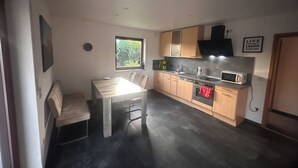 Moderni keittiö, jossa on ruokapöytä, puukaapit, sisäänrakennettu uuni ja ikkuna, josta tulee luonnonvaloa.