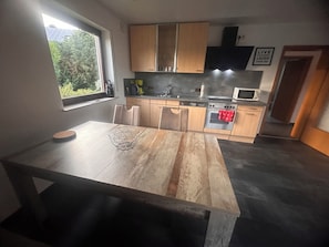 A modern kitchen with wooden cabinets, a dining table, and a window providing a view of greenery outside.
