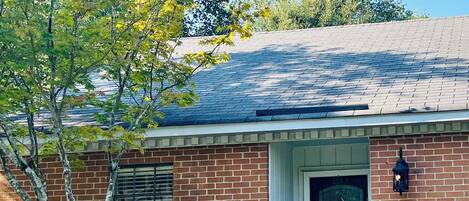 A brick house with a white door and window shutters, a small porch, and a brick chimney.