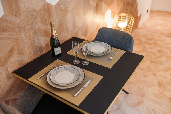 Una mesa de comedor dispuesta con platos, cubiertos y una botella de champán, con una vela al fondo.