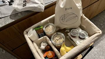 A kitchen counter with a wicker basket containing various food items, including jars of grains, a banana, and a bag of bread.