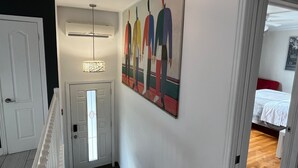 A hallway with a staircase, a painting on the wall, and a bed in the adjacent room.