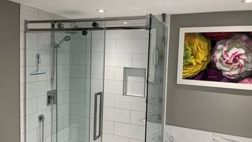 A modern bathroom with a glass-enclosed shower, a white bathtub, and a marble backsplash.