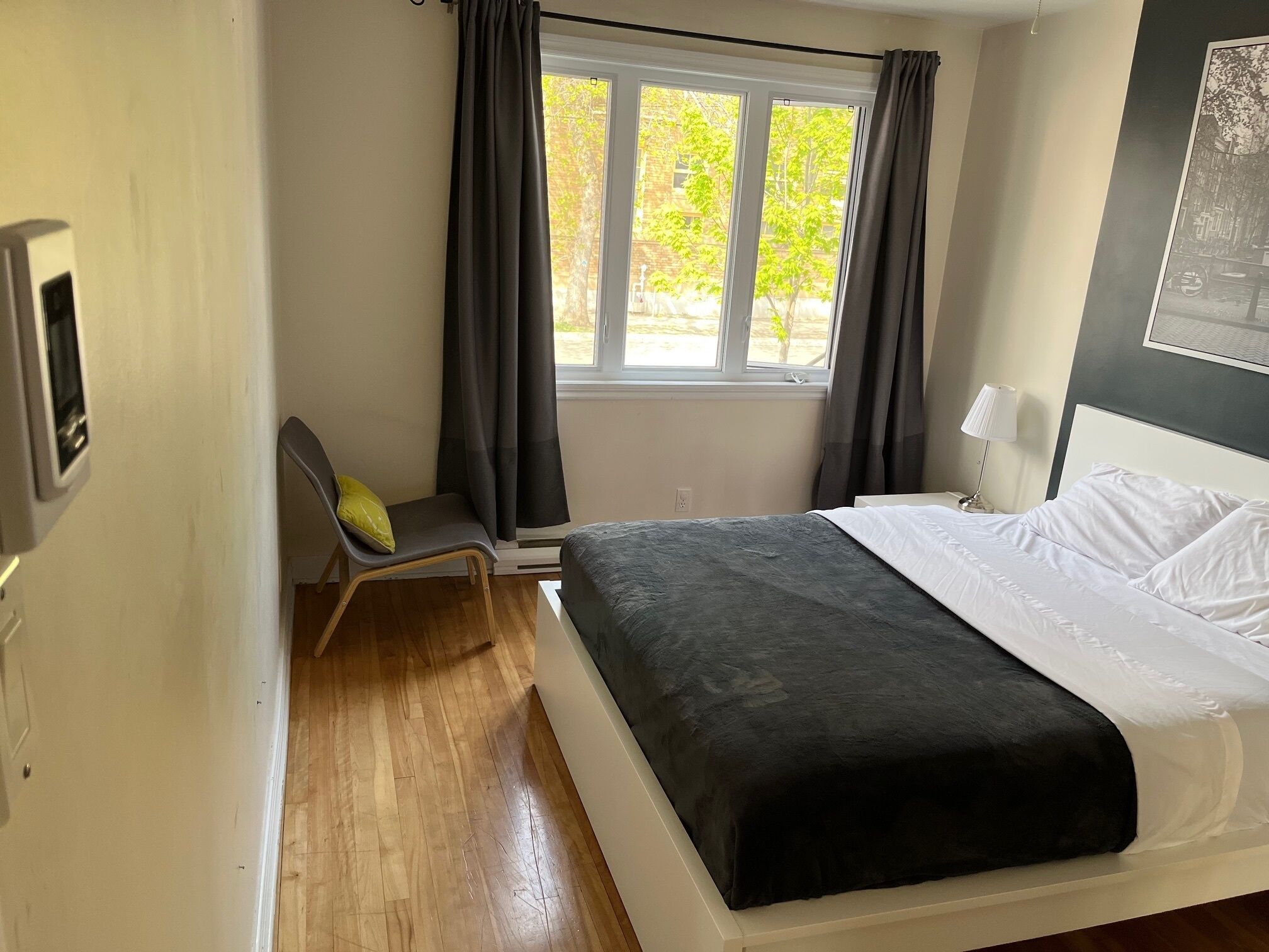 Een slaapkamer met een bed, een stoel, een raam met gordijnen, een lamp en een apparaat aan de muur.