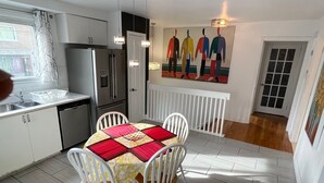 A modern kitchen with white cabinets, a stainless steel refrigerator, and a dining area with a table set for four.