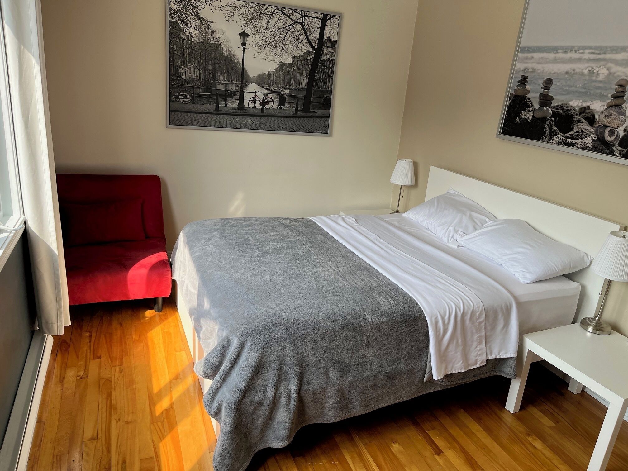 Een hotelkamer met een bed, een rode stoel, een nachtkastje met een lamp, en twee aan de muur hangende foto's.