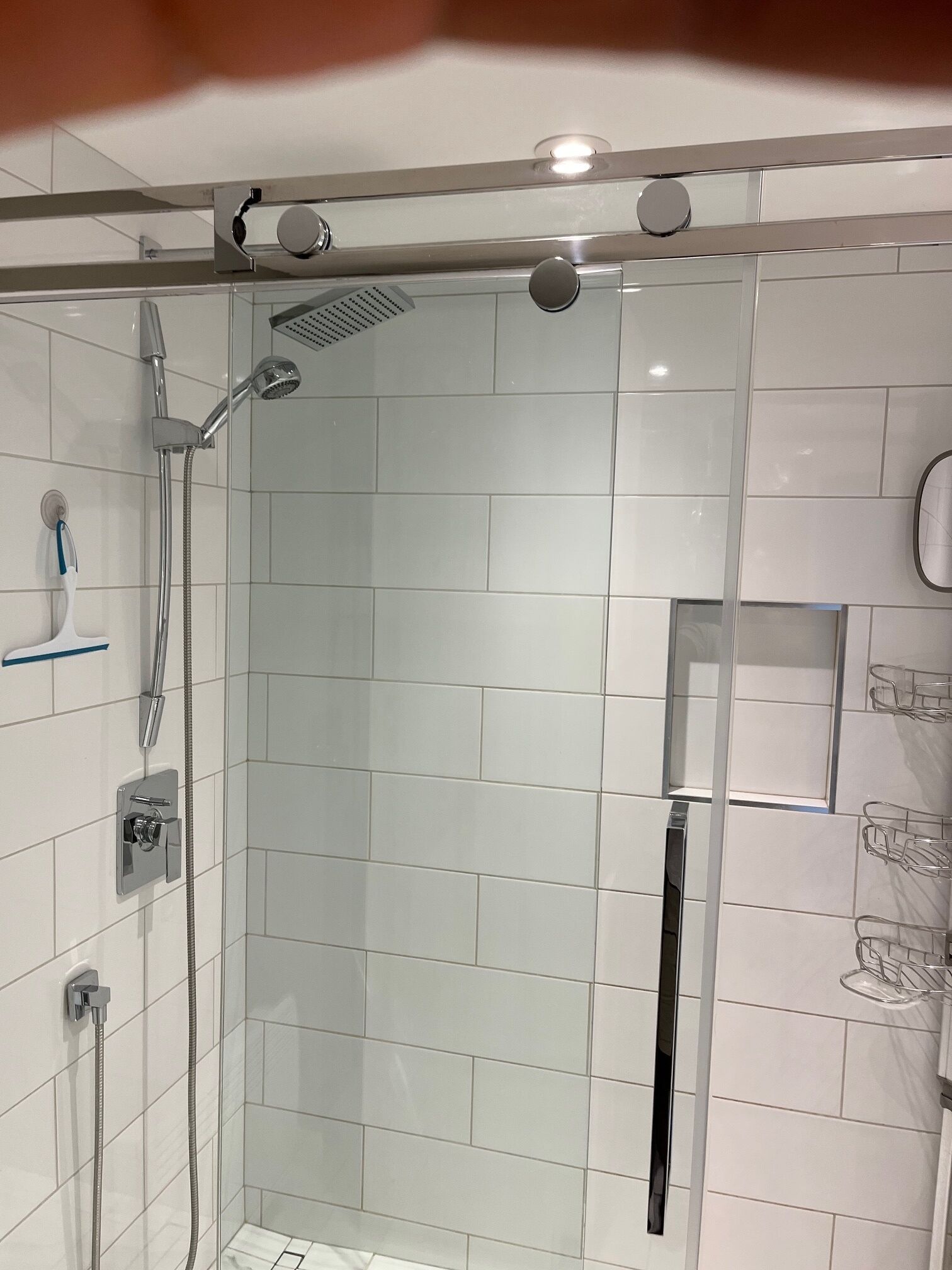 A modern shower with a glass door, a handheld showerhead, and a wall-mounted faucet.