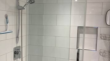 A modern shower with a glass door, a handheld showerhead, and a wall-mounted faucet.