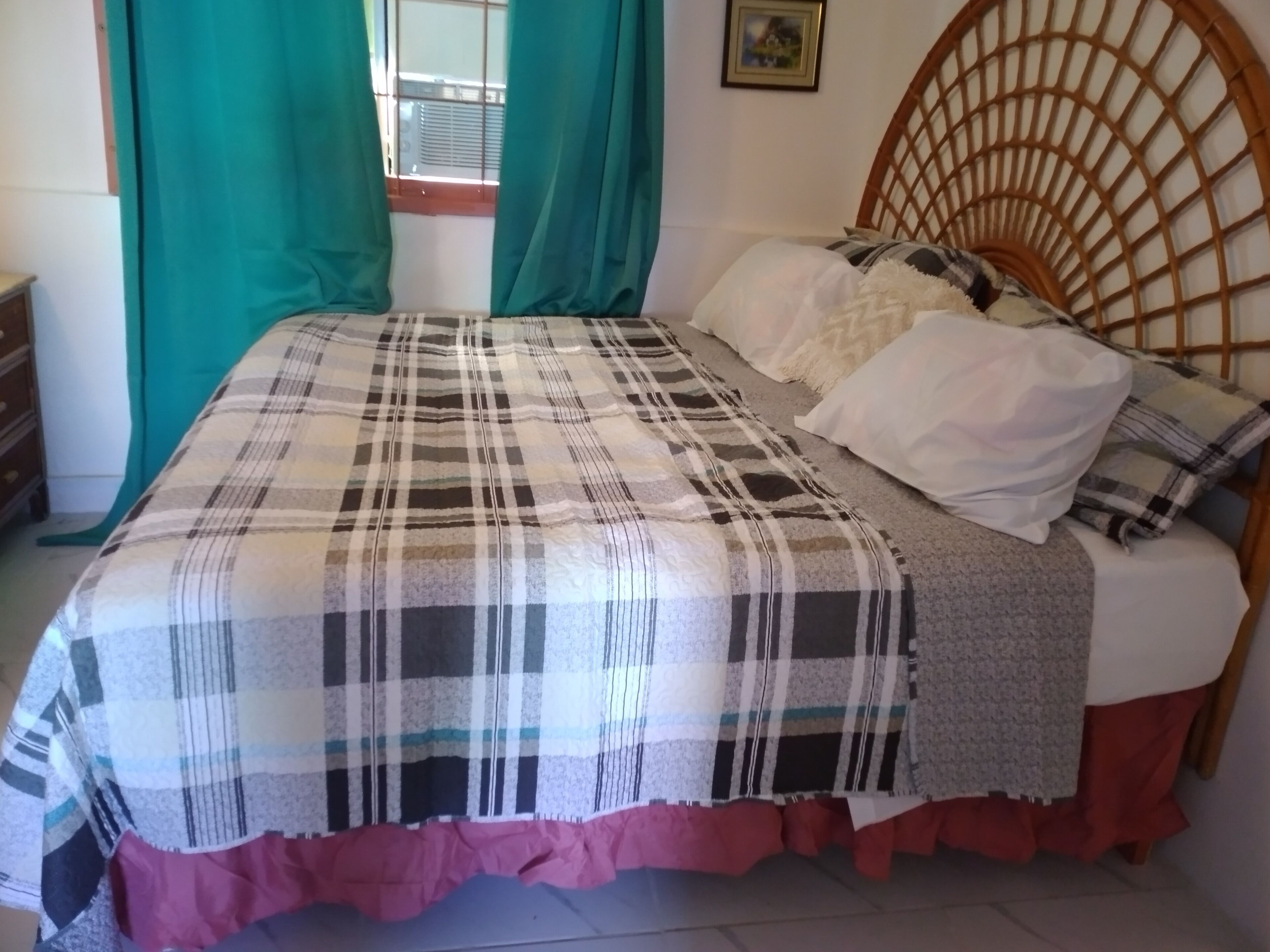 Un lit avec une couvre-lit à carreaux, une tête de lit en bois et une fenêtre avec des rideaux.