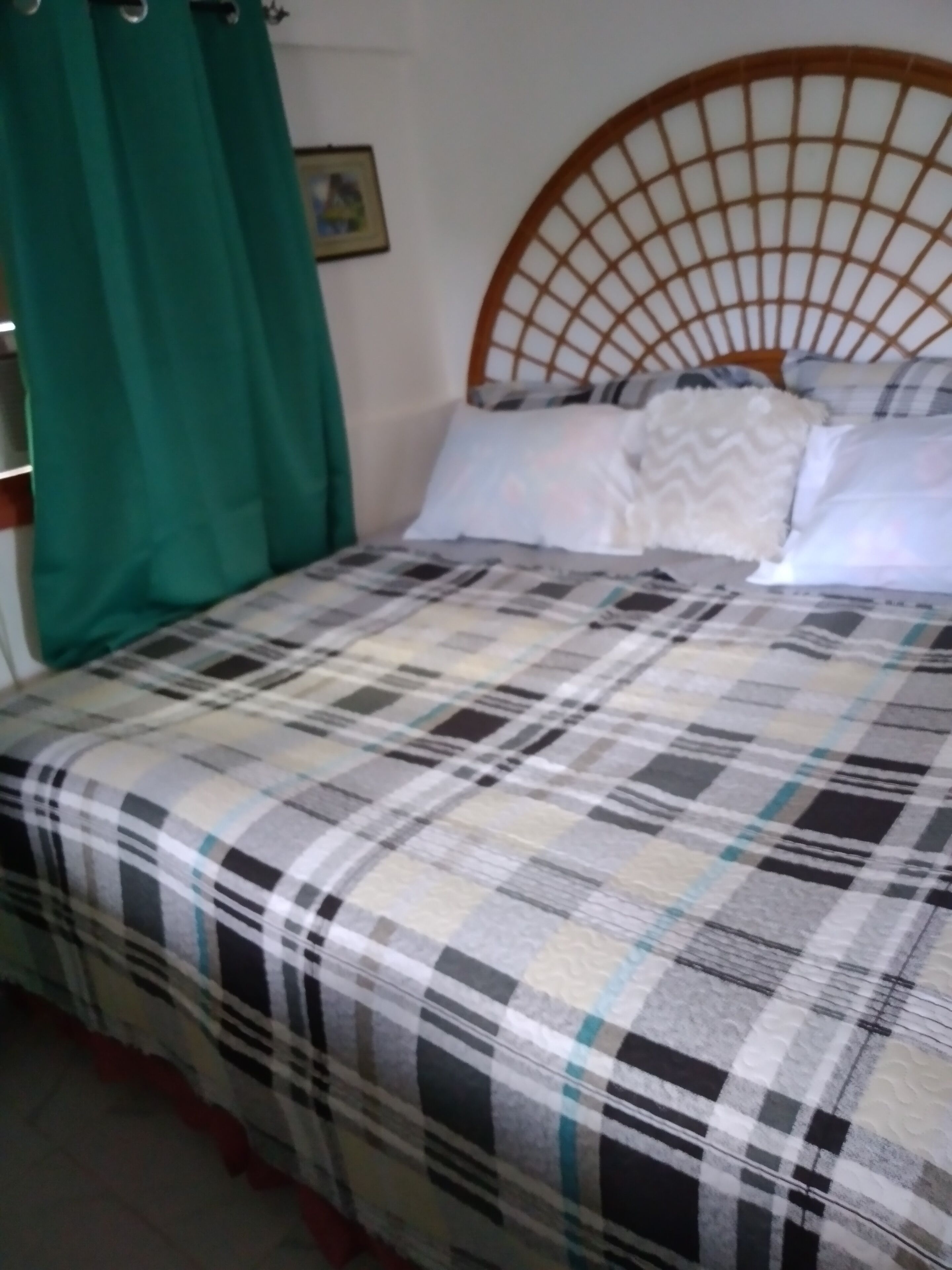 A bed with a checkered bedspread, a wooden headboard, and green curtains.
