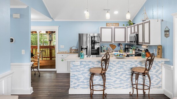A kitchen with a blue and white tiled backsplash, wooden chairs, and a bar area. - Centrally Located Beach Bungalow (Myrtle Beach)