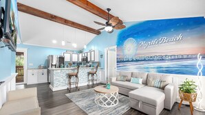 A modern kitchen with white cabinets, a bar area, and a large mural of Myrtle Beach. - Centrally Located Beach Bungalow (Myrtle Beach)