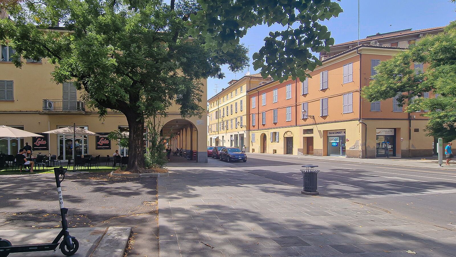 A street with buildings, a scooter, and a trash bin.