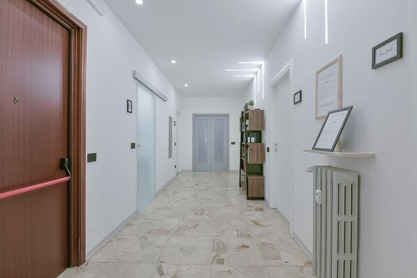 Un pasillo con una puerta de madera a la izquierda, un radiador a la derecha y certificados enmarcados en las paredes.
