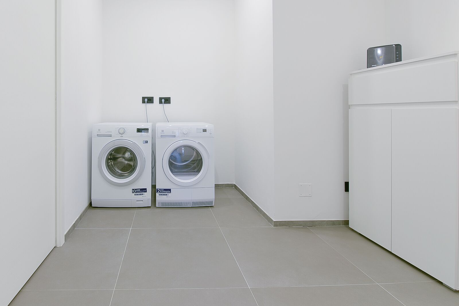 A laundry room with two front-loading washing machines and a white cabinet.