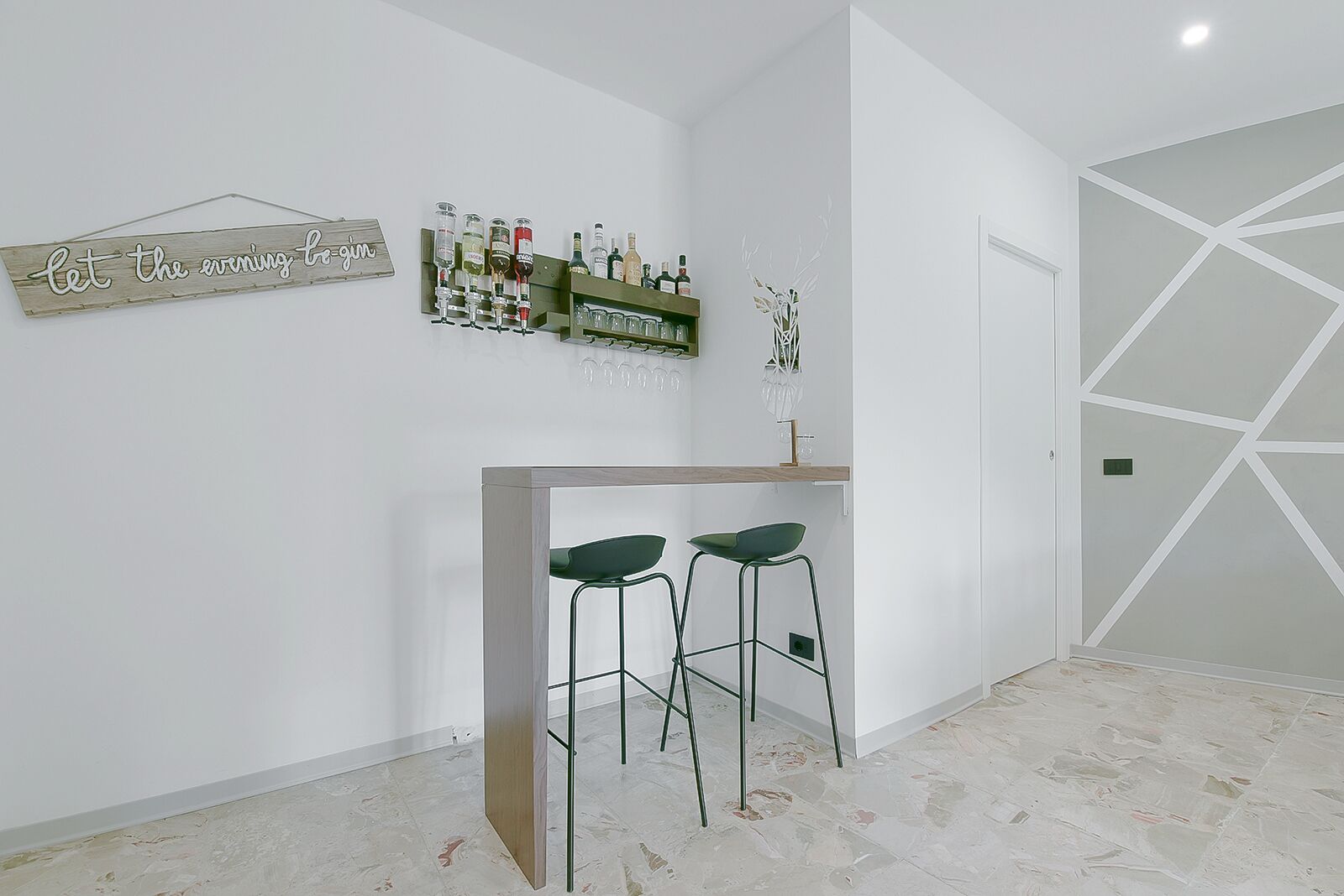 Un área de bar moderna con dos taburetes, una botellera y un cartel decorativo.