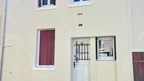 A two-story building with a white facade, numbered 18, featuring a red shuttered window, a white door with a metal gate, and a small window with a metal grill. - Guesthouse close to Disney (Montevrain)