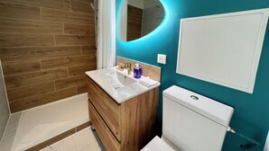 A modern bathroom with a wooden vanity, a white sink, a toilet, and a shower area. - Guesthouse close to Disney (Montevrain)
