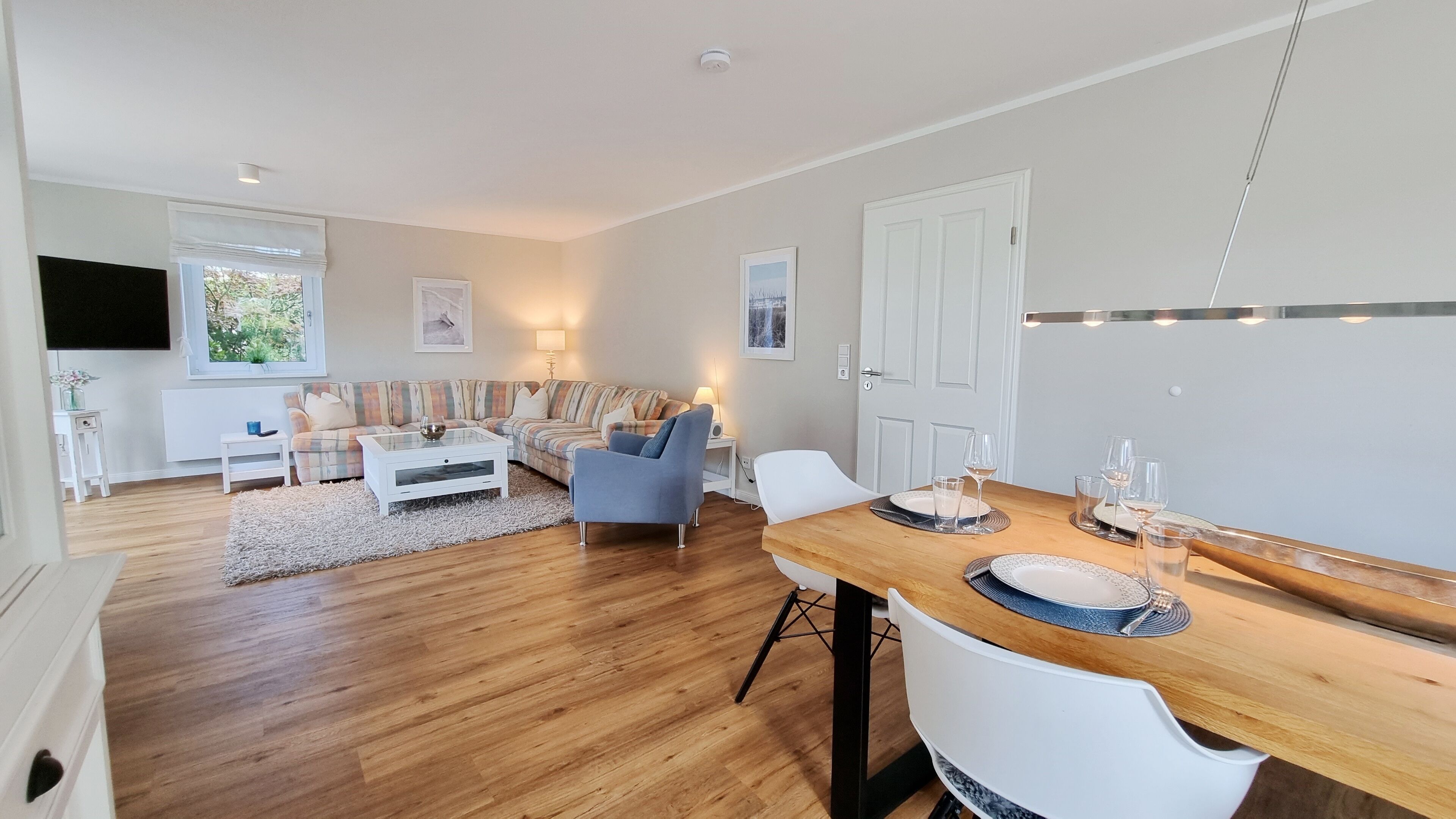 A modern living room with a wooden floor, a sofa, a coffee table, and a dining area with a table set for four.