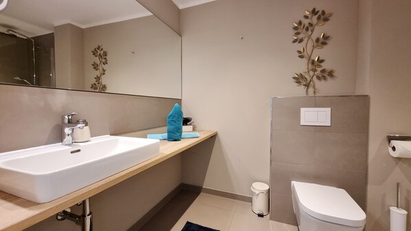 Et moderne badeværelse med en hvid vask, et spejl, et håndklæde, et toilet og en vægmonteret lysarmatur.