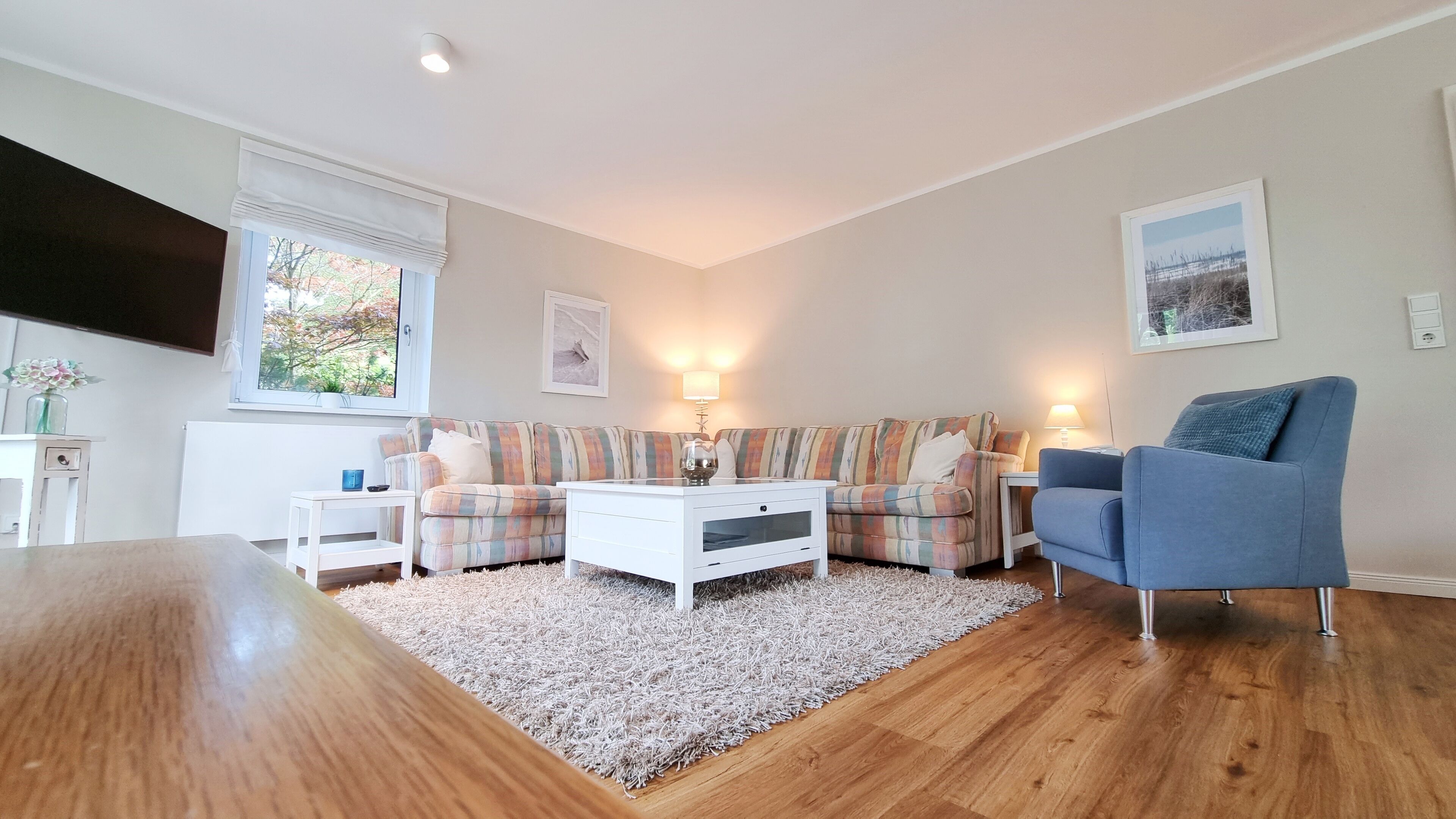 Een woonkamer met een houten salontafel, twee banken, een blauwe fauteuil en een witte vloerkleden.