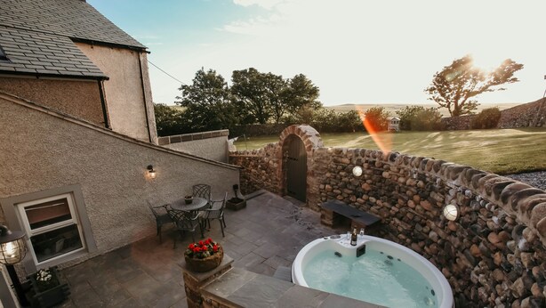 Een stenen muur, een hottub en een terras met stoelen en een tafel.