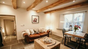 Een gezellige woonkamer met een bruine leren bank, een houten salontafel en een eettafel met stoelen.