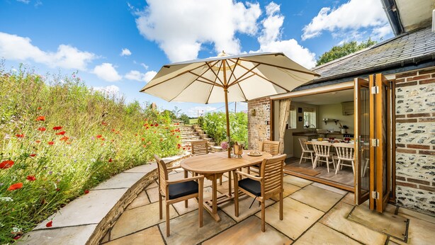 Une terrasse extérieure avec une table et des chaises en bois, un parasol et un mur en briques.