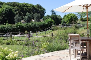 An outdoor patio with a wooden table and chairs, surrounded by lush greenery and a wooden fence. - Cosy Cottage - Chebbard, Dorchester (Dorchester)