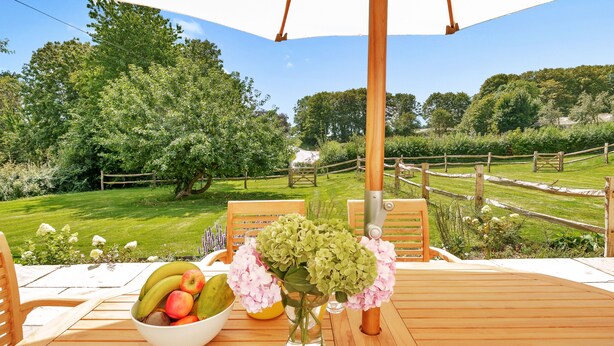 An outdoor wooden deck with a table set for a meal, surrounded by lush greenery and a wooden fence.