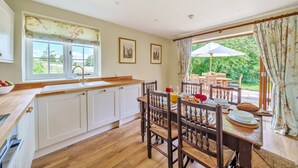 A kitchen with wooden cabinets, a dining table with chairs, and a view of the garden through the window.