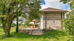 A stone building with a tiled roof, a wooden pergola, and a grassy lawn.