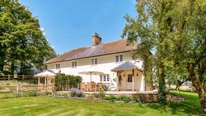 A large, two-story house with a well-maintained lawn, outdoor seating area, and a small garden.