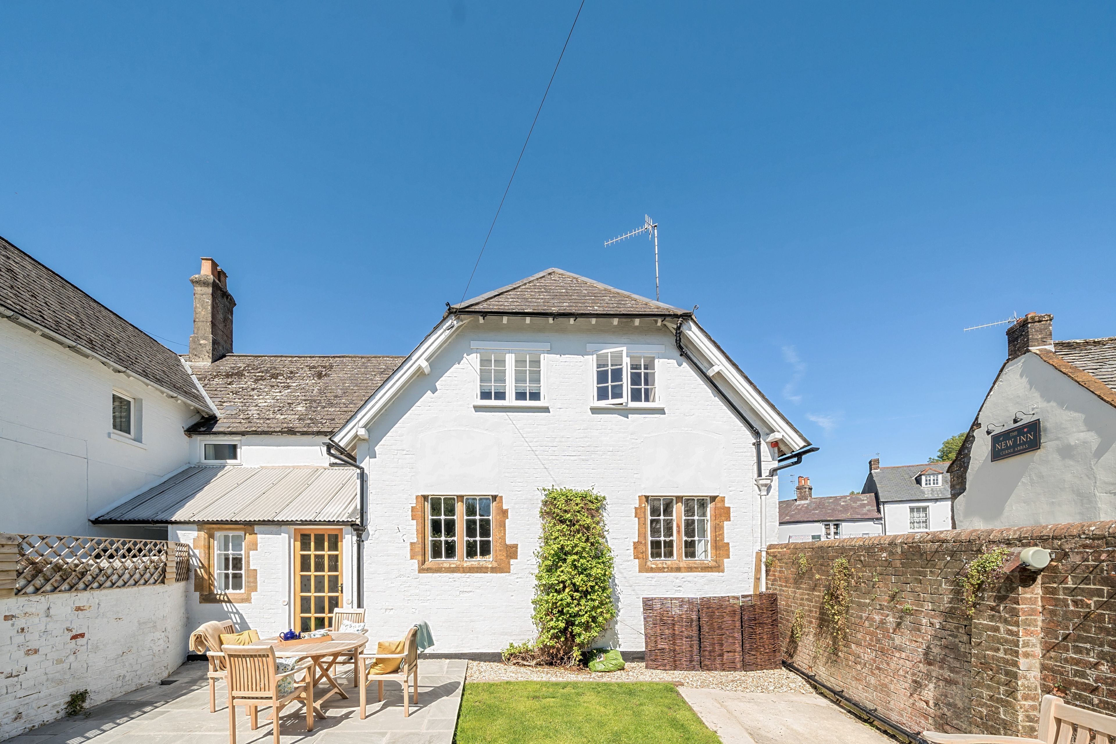 A white house with a tiled roof, a chimney, and a small garden with a table and chairs.