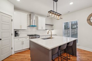 A modern kitchen with white cabinetry, a central island with bar stools, a stainless steel range hood, and a pendant light. - Luxurious home in the heart of Downtown Nashville (Nashville)