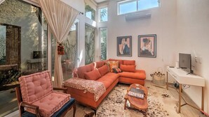 A modern living room with a sectional sofa, a pink armchair, a coffee table, and a TV on a white desk.