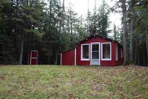 Punainen mökki, jossa on valkoinen ovi ja ikkunat, ja sen ympärillä on metsää.