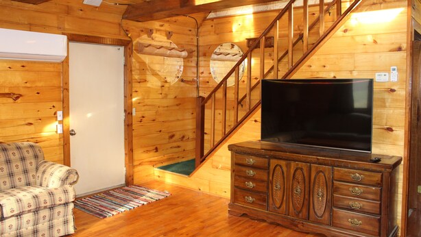 L’intérieur d’un chalet en bois, avec un canapé à carreaux, un meuble de rangement en bois abritant un téléviseur et un escalier.