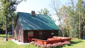 Une cabane avec un toit en métal vert, une terrasse et un jardin agrémenté de fleurs roses.