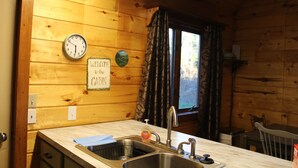 Une cuisine rustique aménagée dans une cabane en bois, avec un évier à deux bacs, une horloge et une pancarte de bienvenue.