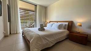 Une chambre d’hôtel avec un grand lit, une table de chevet en bois, une lampe et une vue par la fenêtre.