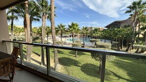 A balcony with a view of a pool area, palm trees, and a building in the background. - Herdade dos Salgados, T1 6B_1C, Vila das Lagoas (Albufeira)