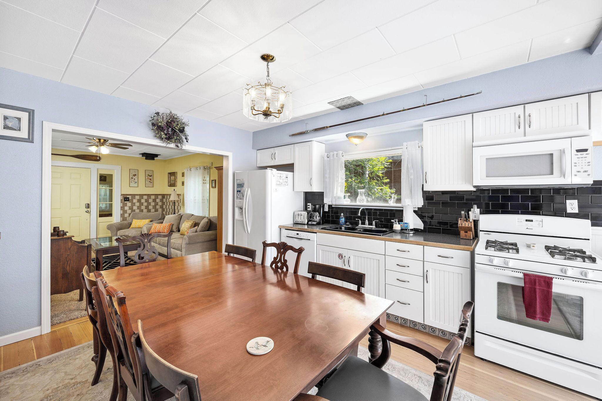 A modern kitchen with white cabinetry, a wooden dining table, and a chandelier.