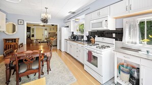 A modern kitchen with white cabinetry, a dining area with a wooden table and chairs, and a view of the outdoors through a window. - Peaceful home in downtown CDA, 4 bed/2 bath!  Enjoy the sun on the private deck! (Coeur d'Alene)