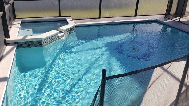Piscina com água cristalina, banheira de hidromassagem e cerca de proteção.