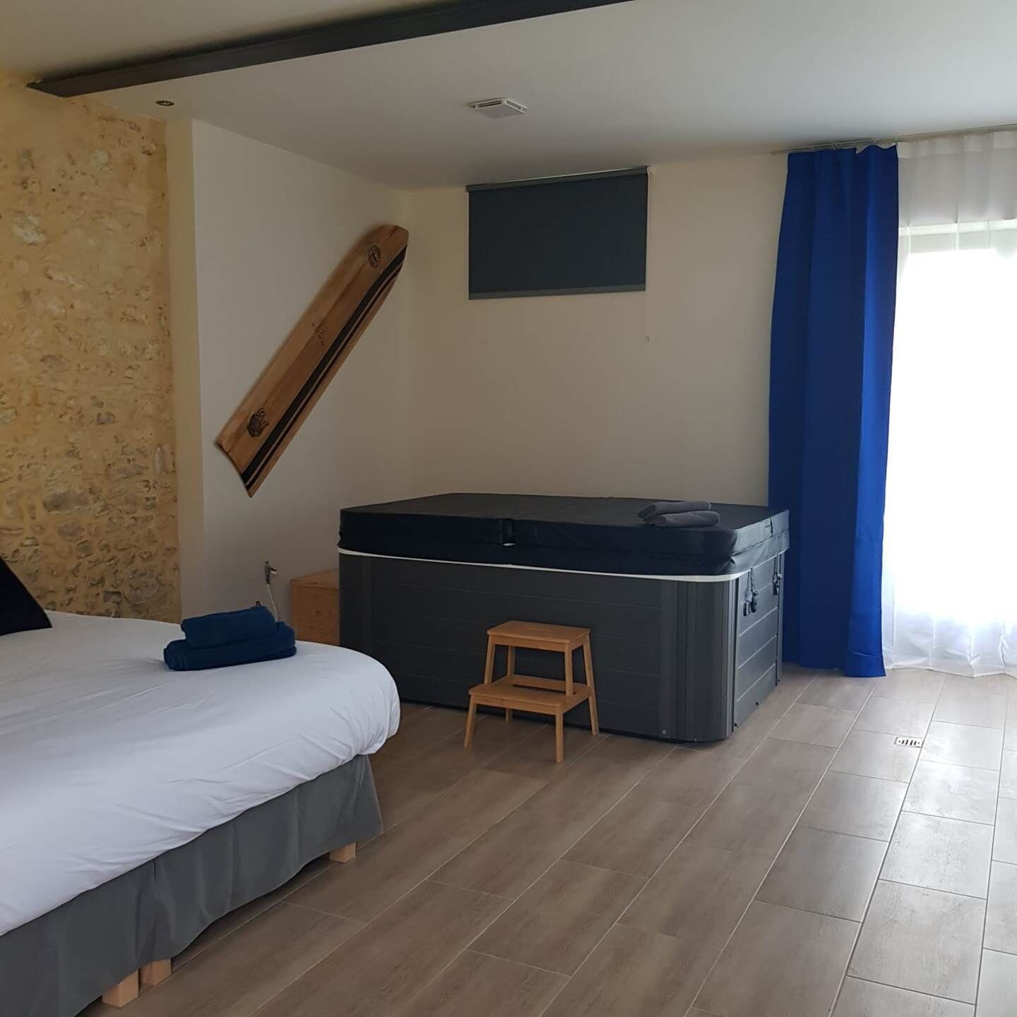 A bedroom with a bed, a hot tub, a small wooden stool, and a stone wall.