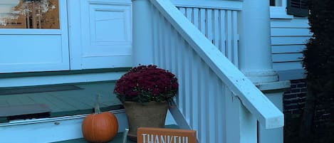 Eine Veranda mit einem Schild, auf dem 'THANKFUL Grateful Blessings' steht, zwei Kübelpflanzen und drei Kürbisse.
