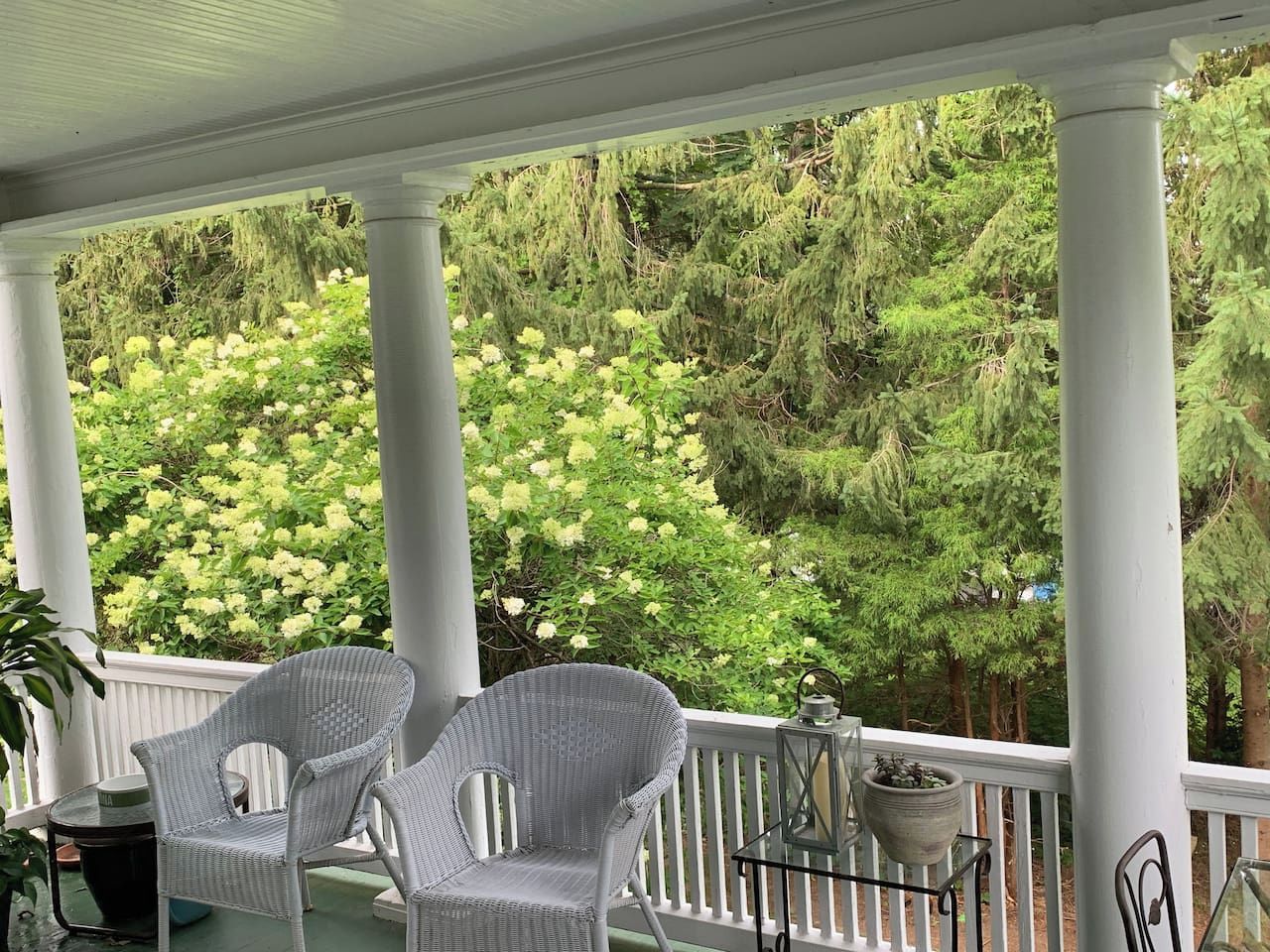A covered porch with two wicker chairs, a small table, and a lantern.